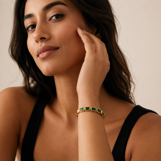 Woman wearing a gold bracelet with green stones on a neutral background
