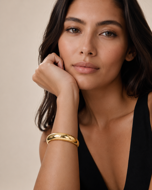 Woman wearing a gold bracelet on a beige background